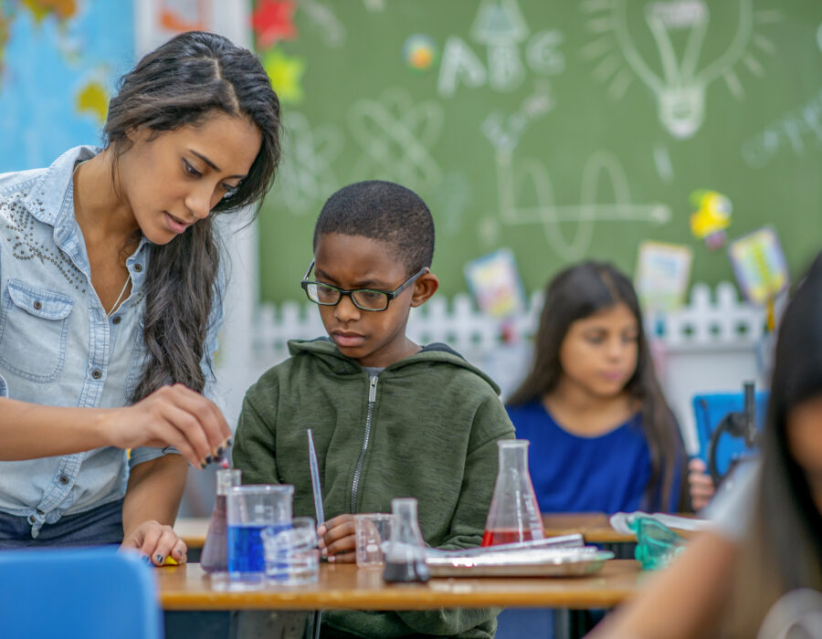 Photo of a young woman teacher helping a boy in her class with a chemistry experiment.