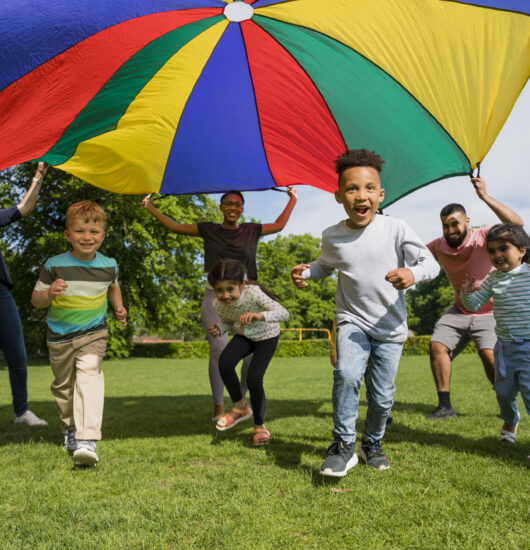 Children playing with a parachute at preschool. The children are running underneath it.