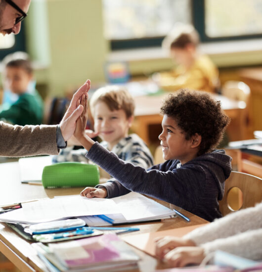 Happy man teacher giving high-five to his elementary student in the classroom.