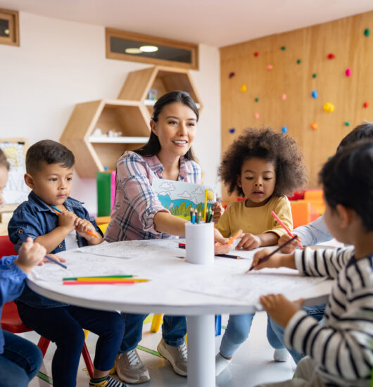 Photo of happy group of young children coloring in art class under the supervision of their teacher.