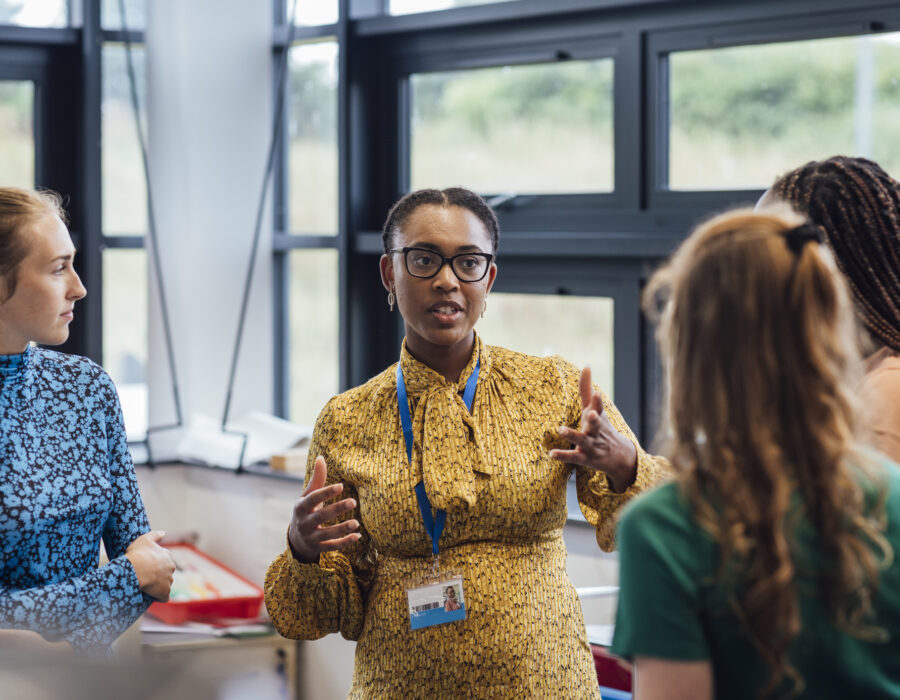 Photo of a secondary school teacher talking with her students in a warm and open manner in class.