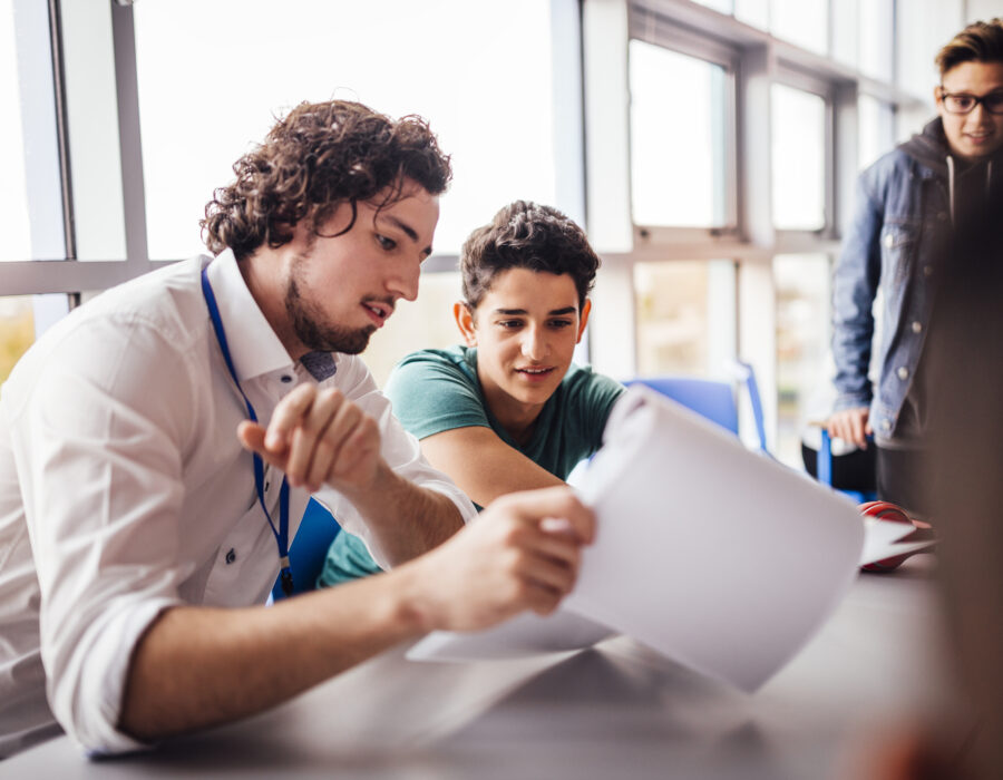 Photo of teacher showing a student some results on his paperwork. The student looks happy as they sit side by side at a table.