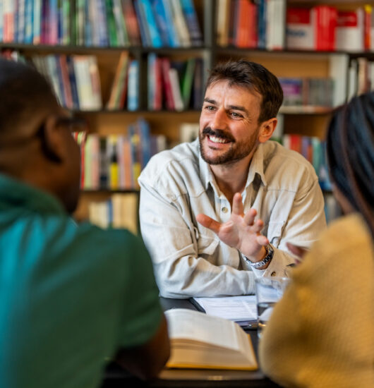 Smiling administrator talking with students around a library desk